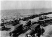 Black and white photo of cars and people crowding the beach