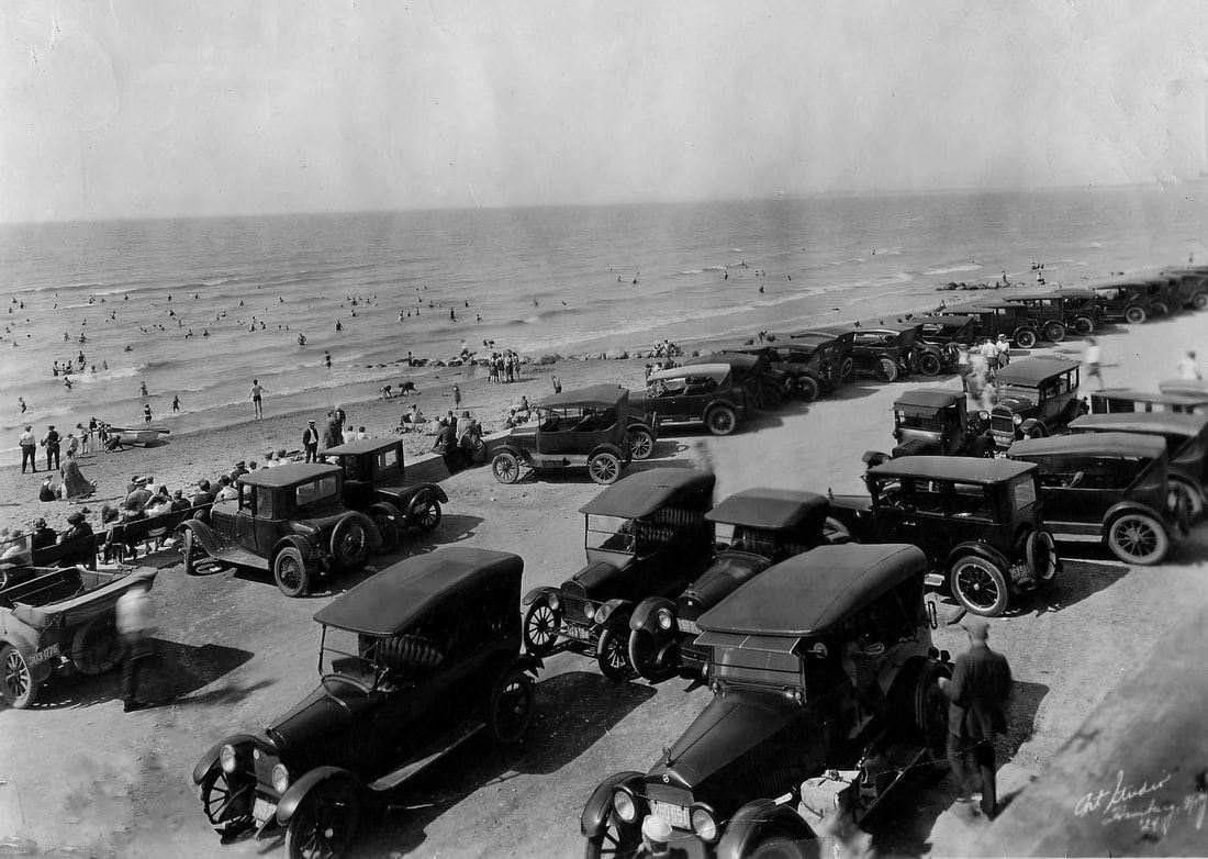 Black and white photo of cars and people crowding the beach