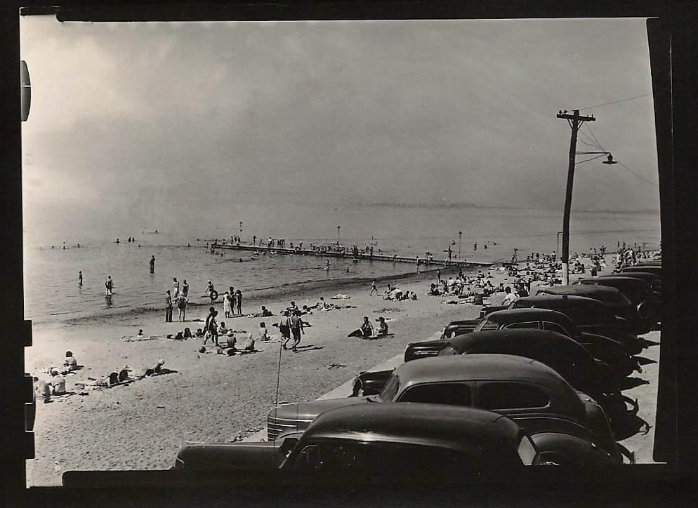 Black and white photo of cars lined up and people at the beach